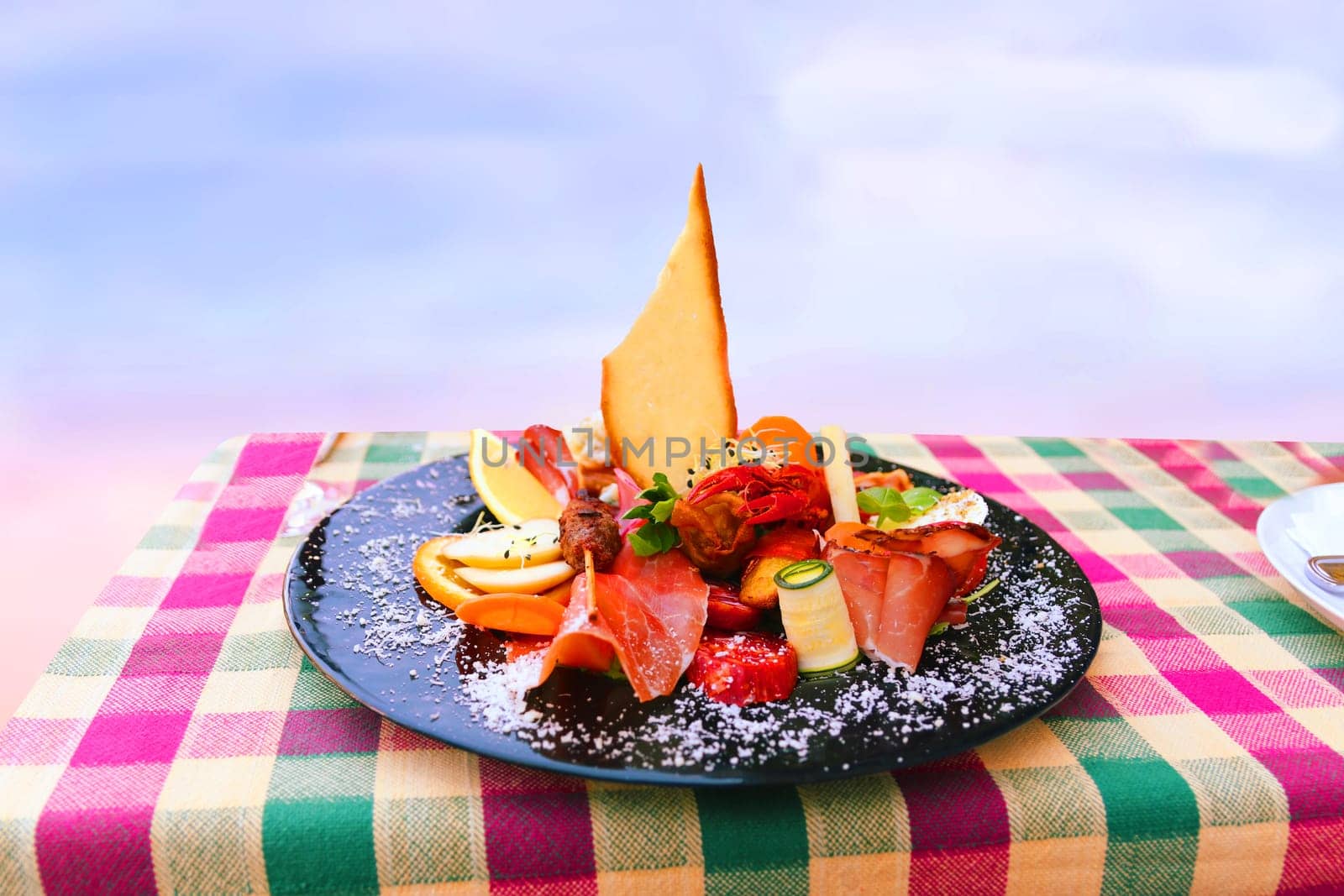 Traditional Italian food. Close-up of mixed Mediterranean appetizers or antipasto and tapas with ham vegetables and crab on black plate on table over bright background. Space.