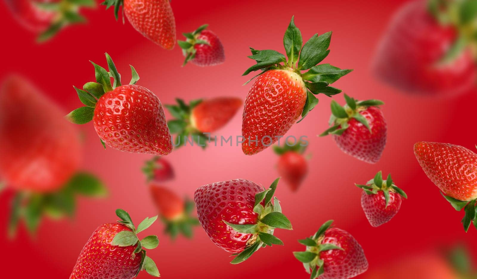 Ripe red strawberries with green leaves levitate on a red background, a sense of perspective