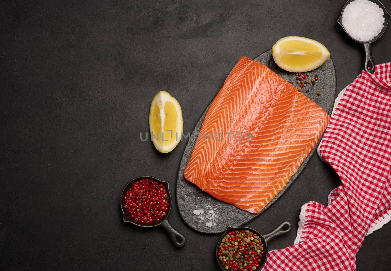 Raw piece of trout on a black board and spices, top view. Copy space