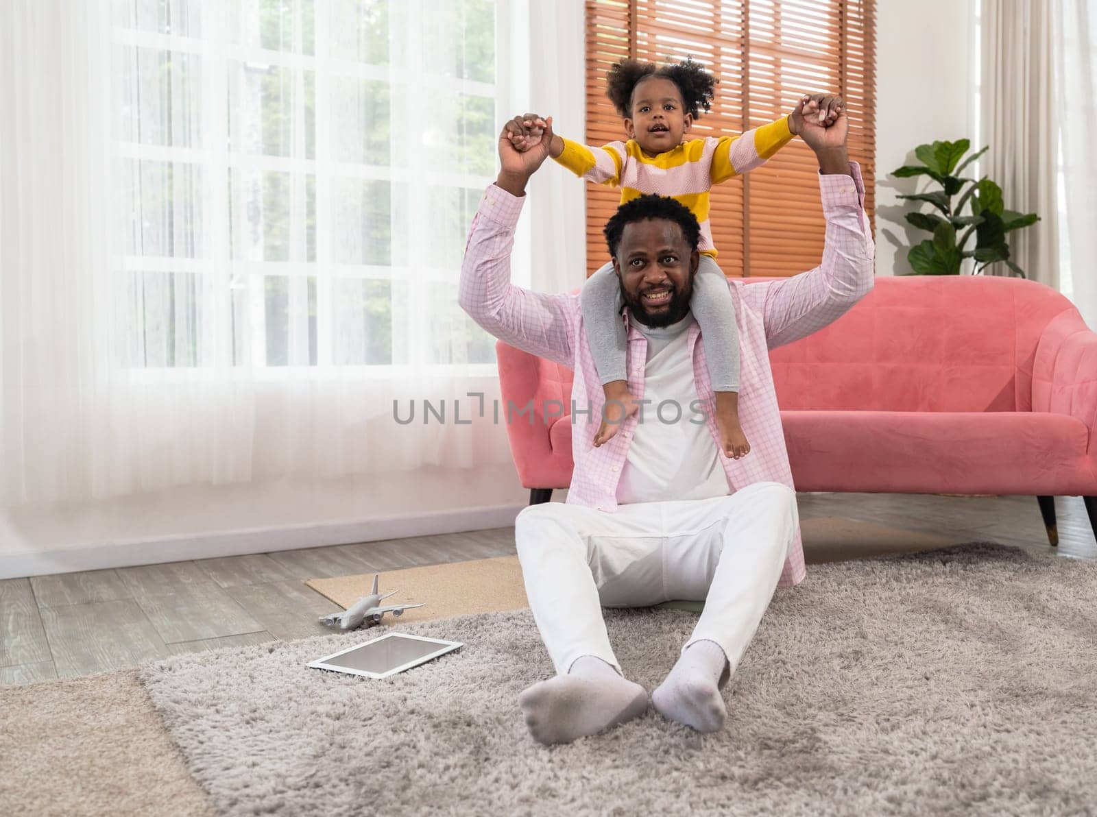 Cheerful African father carrying on neck playing with happy little curly preschool child daughter in living room. Playful small kid girl having fun with smiling bearded dad at home. Happy loving family relations concept.