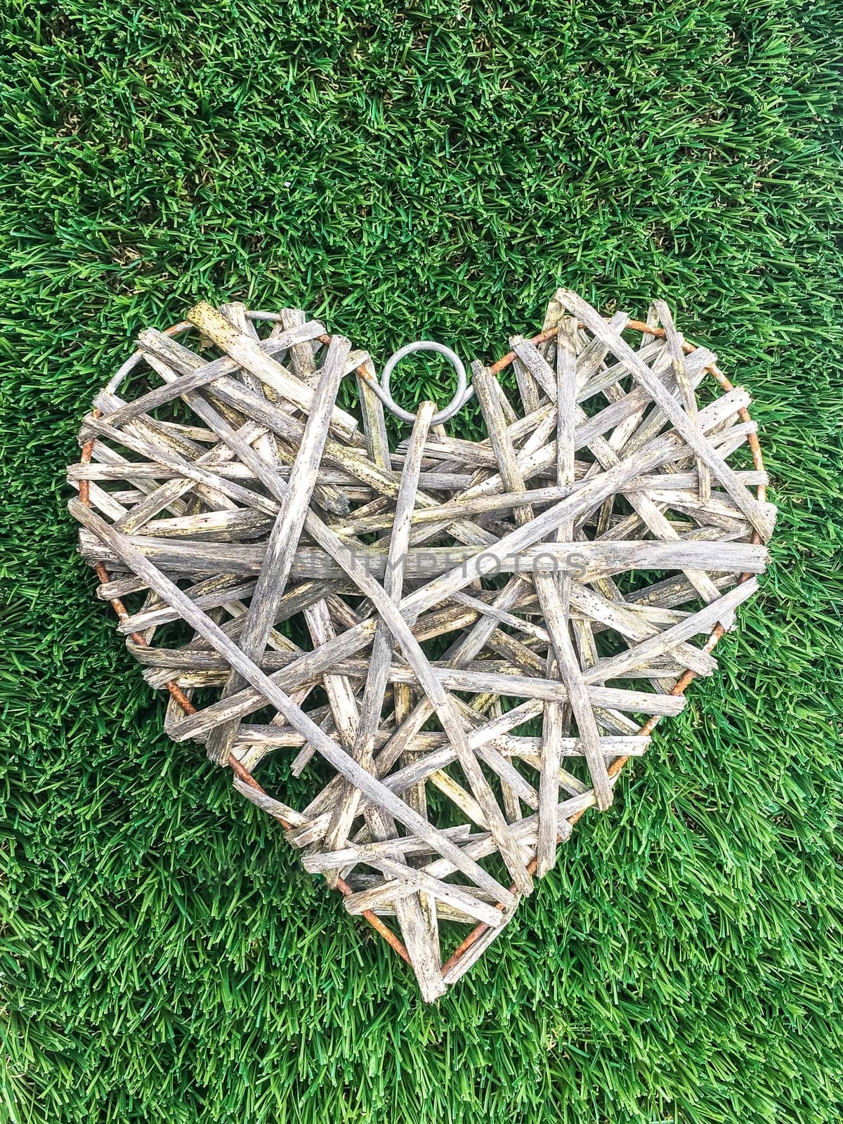 Wicker heart is on a green grass on a sunny day. Romantic background for a declaration of love, announcement of an engagement or other amorous event. Valentine. Event. San Valentine.