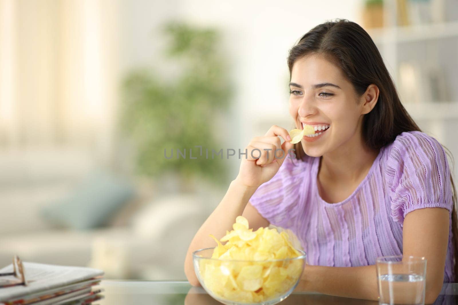Happy woman laughing and eating potato chips alone at home
