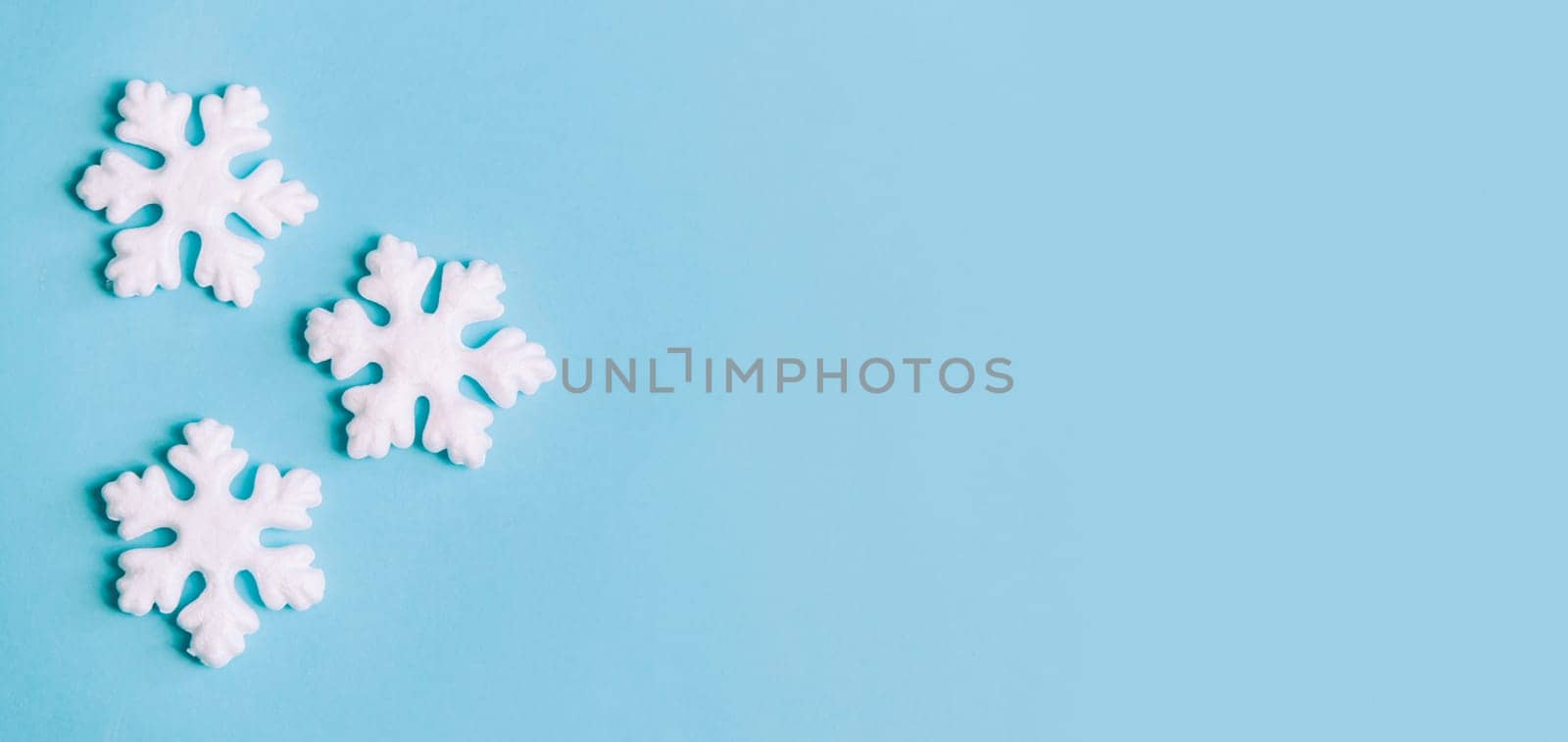 Minimal christmas, new year and winter holiday composition. Flat lay. Creative banner with snow flakes on pastel blue background. Christmas and wintertime concept. Top view.