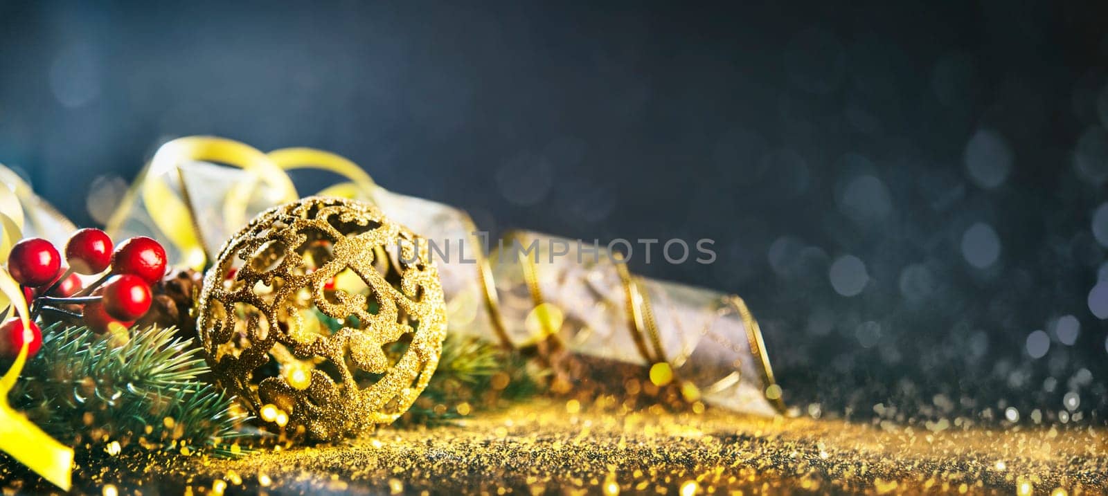 Golden chrismtas ornament ball with fir tree and gold ribbon on dark bokeh glitter background. Happy new year greeting card design. Luxury celebration decor banner layout.