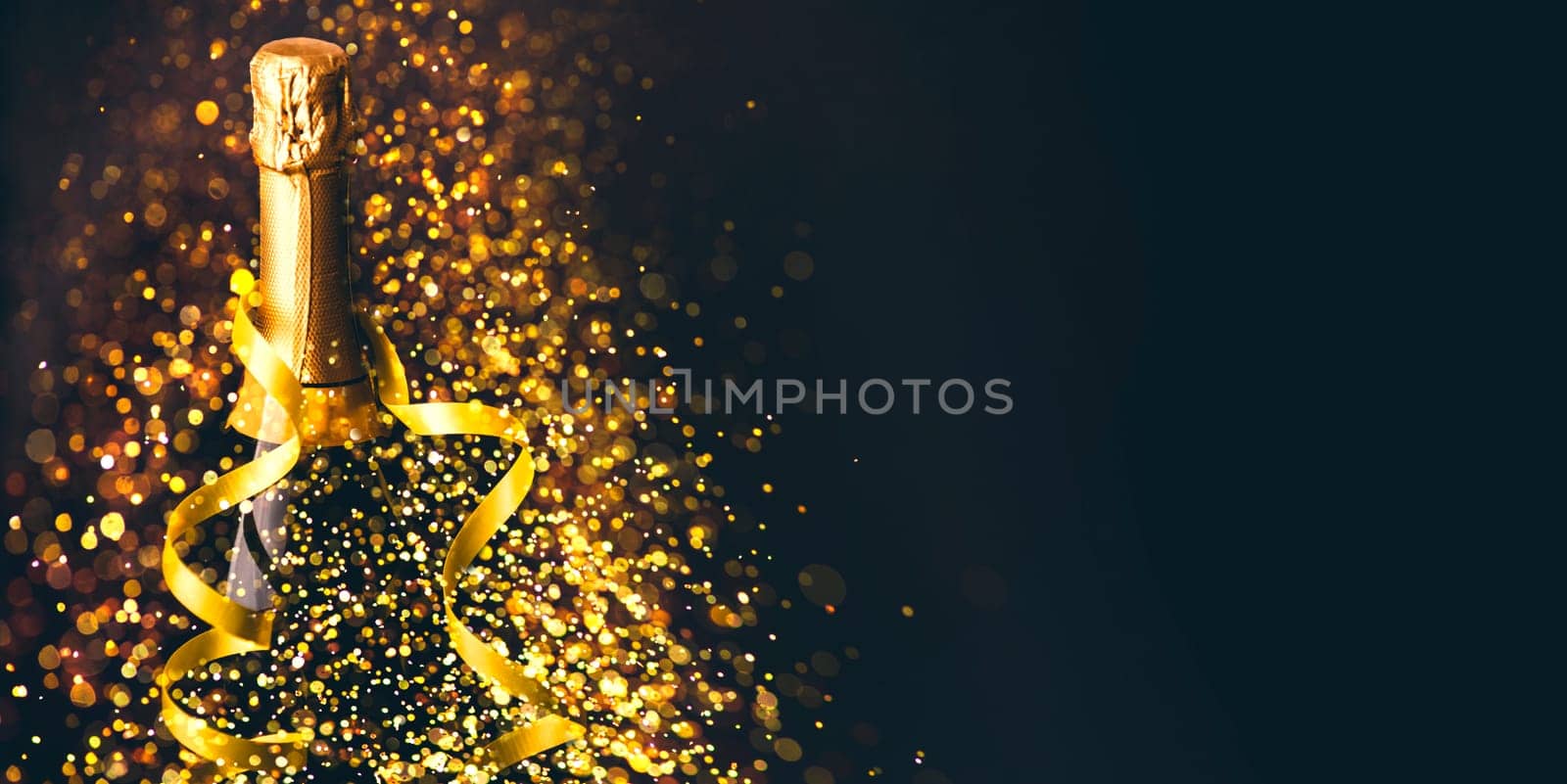 Luxury new year background. Champagne bottle with gold ribbon on dark background with golden bokeh glitter firework. Christmas celebration panoramic design banner.
