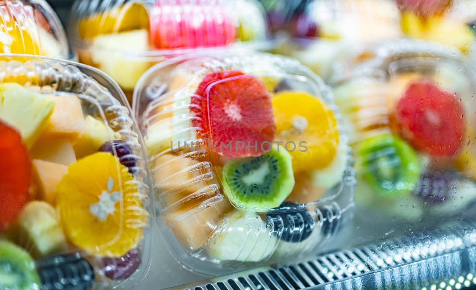 Plastic boxes with fresh fruits displayed in a commercial refrigerator. Fruit salad