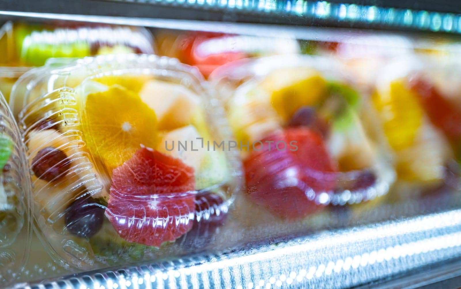 Plastic boxes with fresh fruits displayed in a commercial refrigerator. Fruit salad