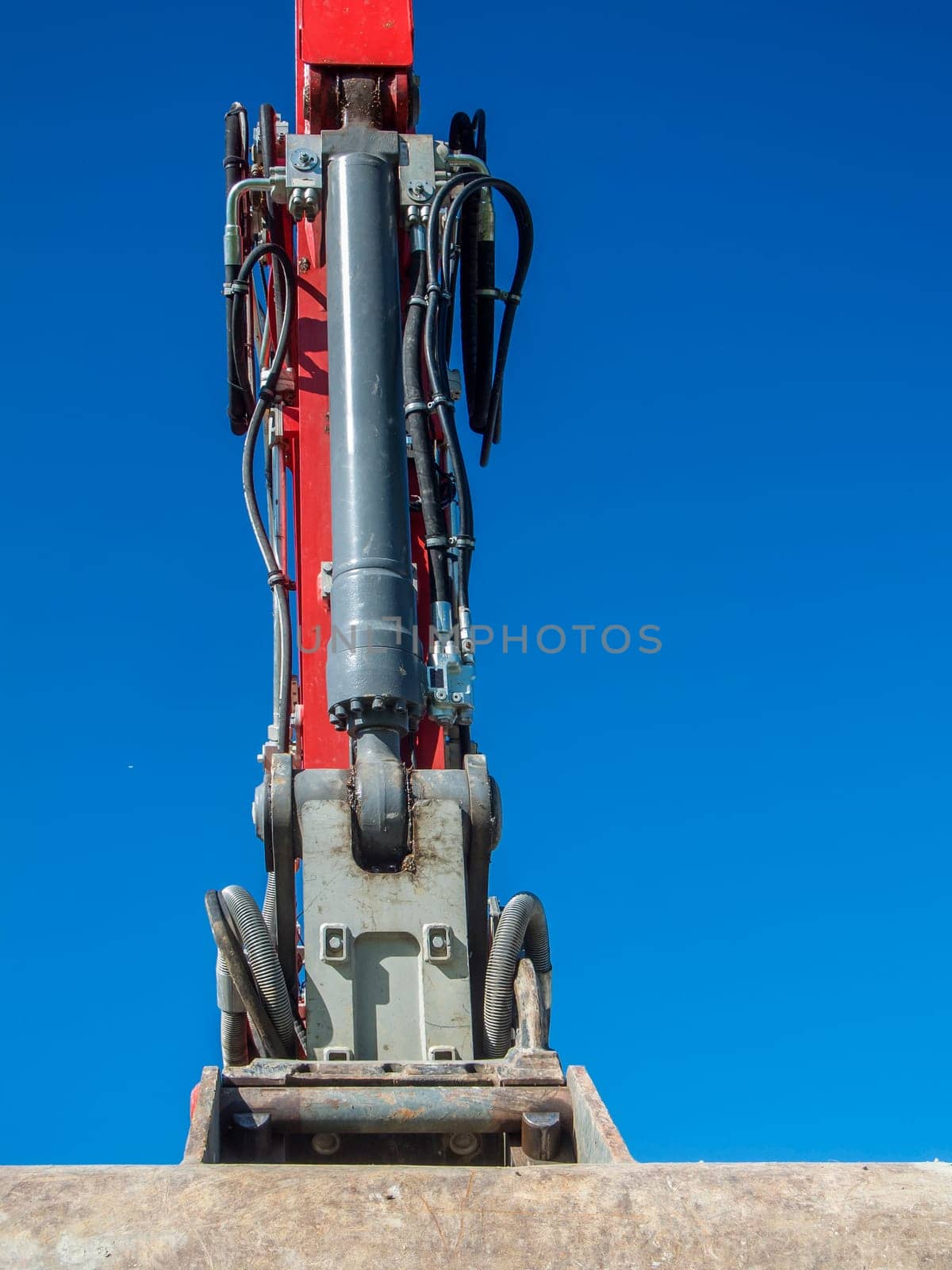 Front view of the boom of an excavator with a bucket against a blue sky.