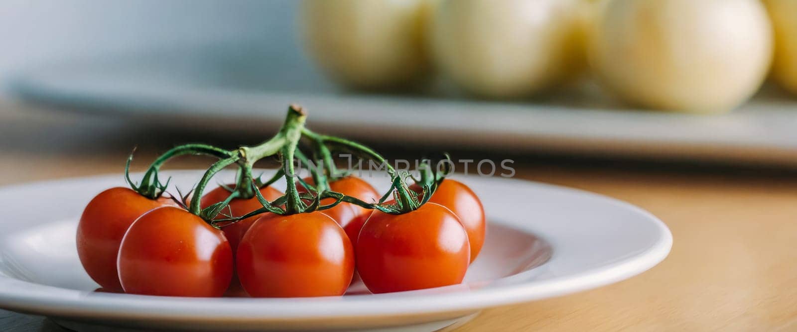 Close-up of fresh cherry tomatoes on a vine, placed on a white plate with a blurred background, highlighting their vibrant color and freshness.