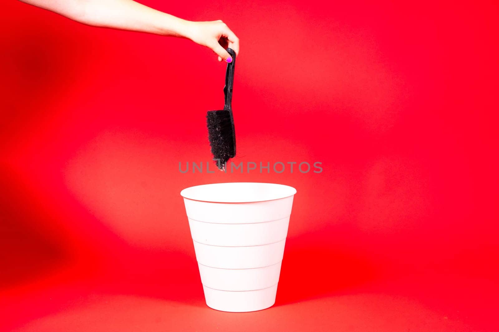 Hand throws brush into trash bin with package on a red background