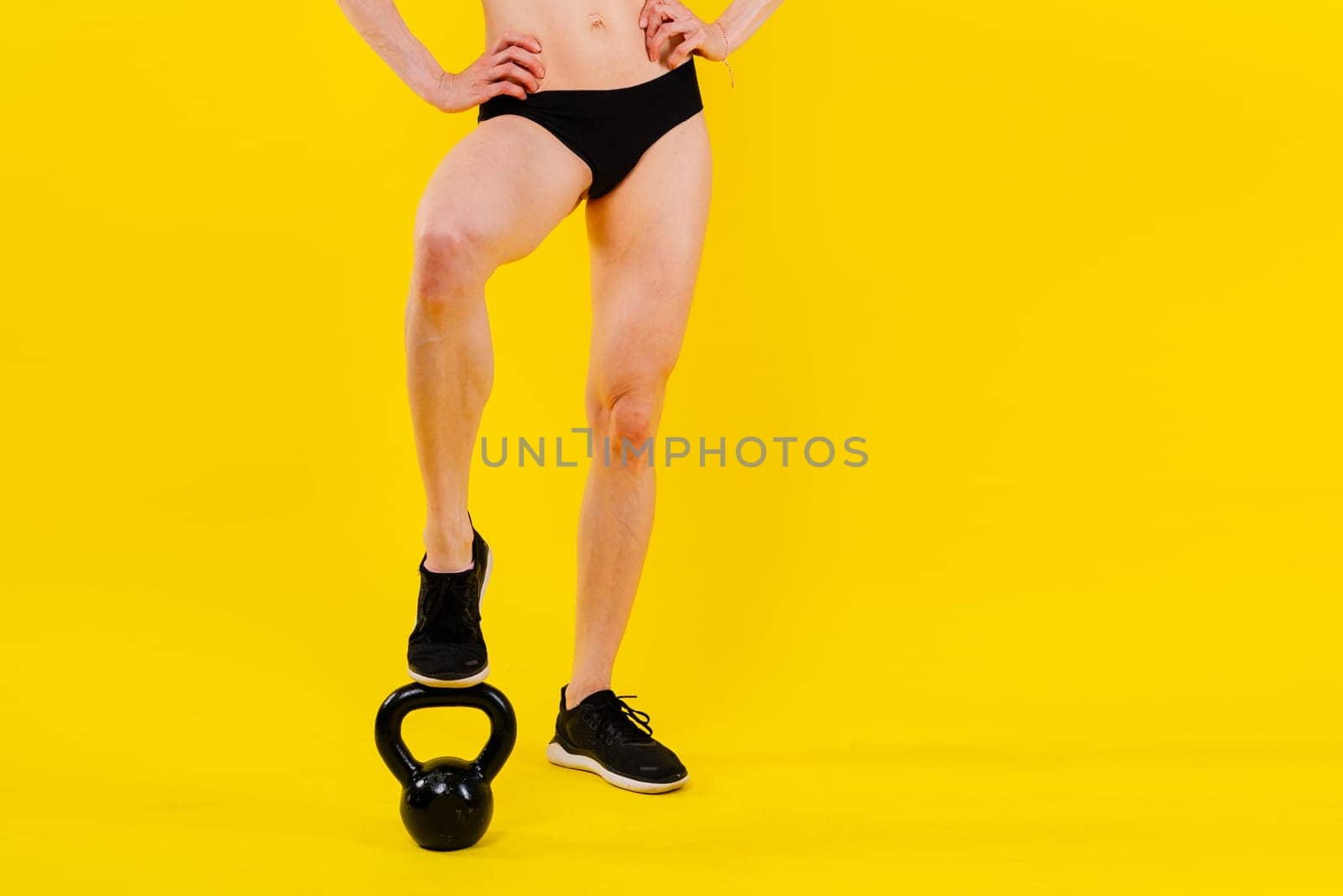 Tough fitness female model with kettle bell on a grey dark yellow red background.