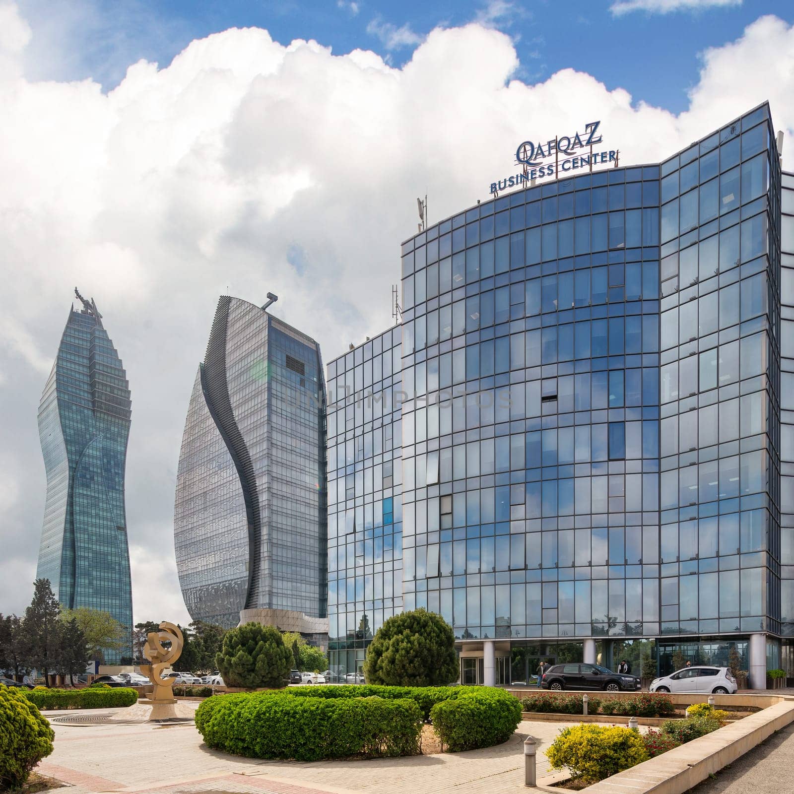 Baku, Azerbaijan - May 7, 2024: Qafqaz Business Center, a modern glass building against a backdrop of skyscrapers and a blue sky with white clouds