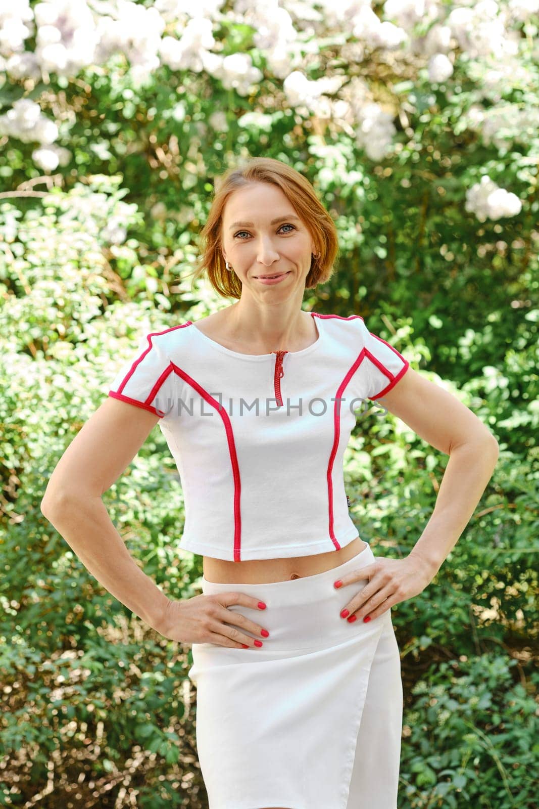 Smiling redhead woman in tennis outfit holds hands on her waist