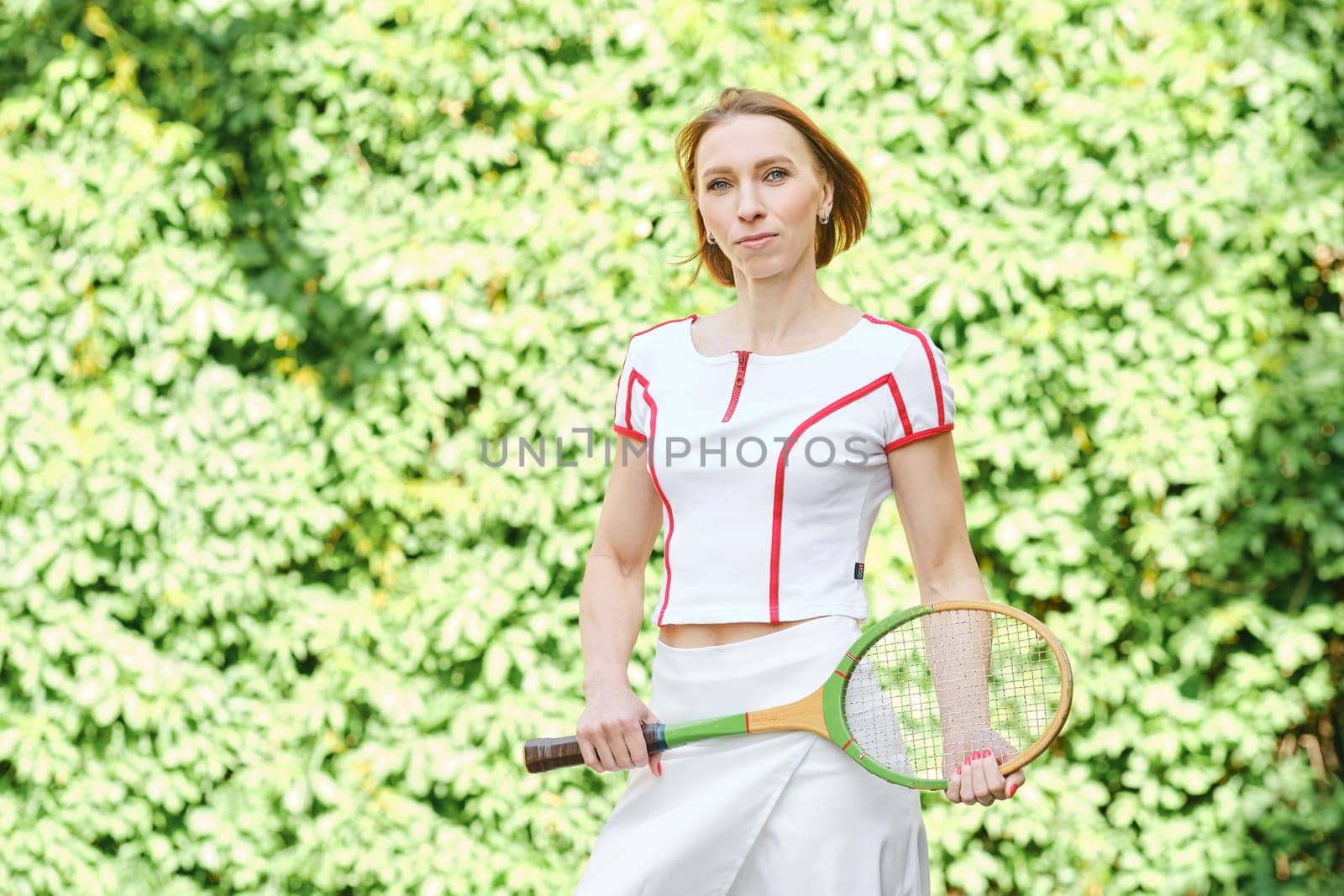 Adult redhead woman in tennis outfit posing with tennis racket
