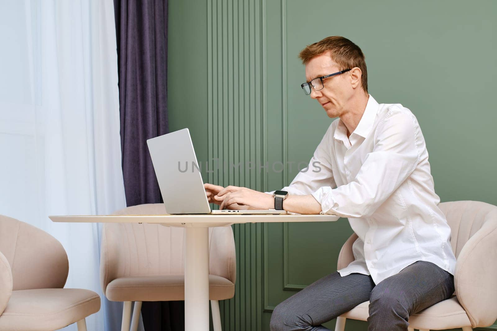 Middle aged man in casual white shirt and grey trousers working online at home