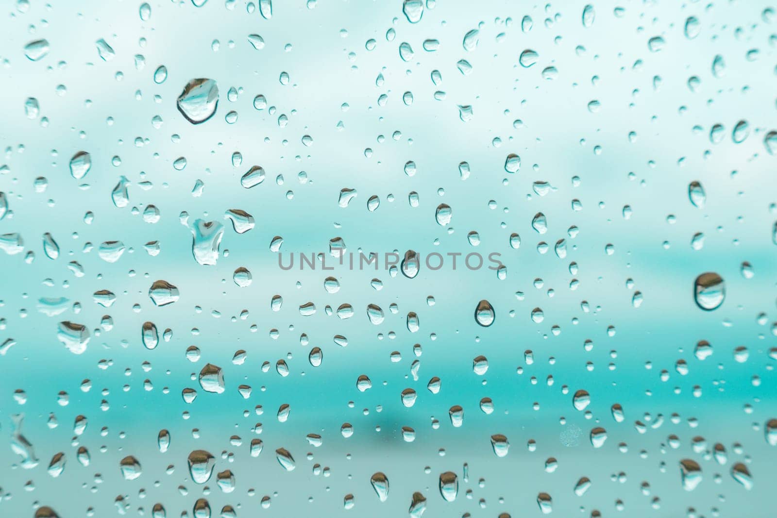 Drops on a window glass with blurry blue background close up , rain macro