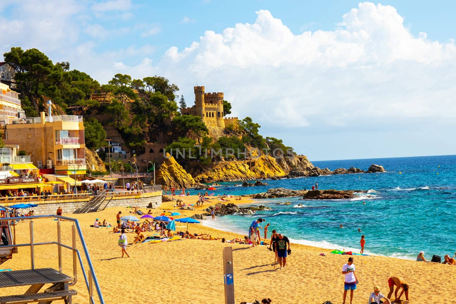 Lloret de Mar, Catalonia, Spain, 02 October 2019. Tourists on the beach of Lloret de Mar below the Castell de Plaja, a castle-like house from the 1940s. Costa Brava.