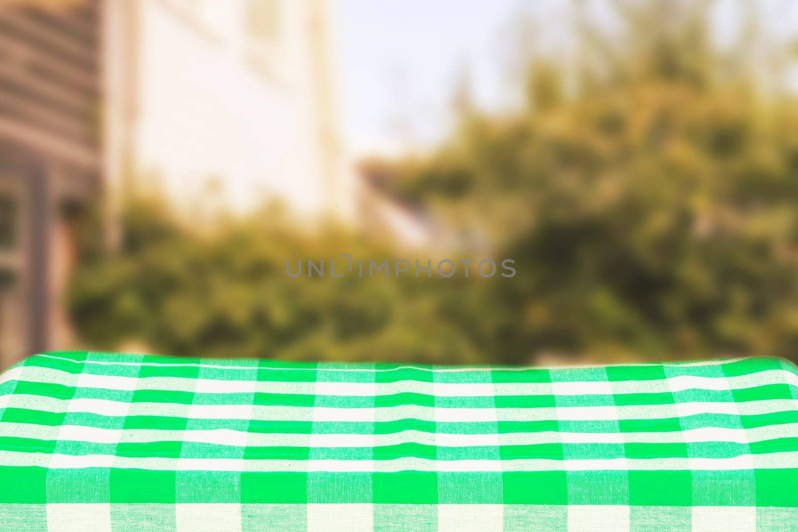 Empty table product. Empty colorful checkered tablecloth over abstract blurred natural green background texture with space for food and product display montage.