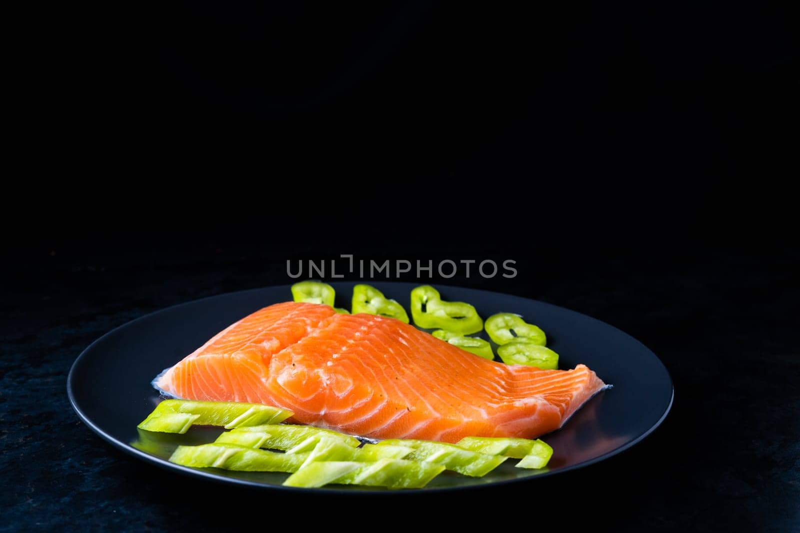 Salted fish salmon with pepper and onions on black plate. Top view. Free space for your text.