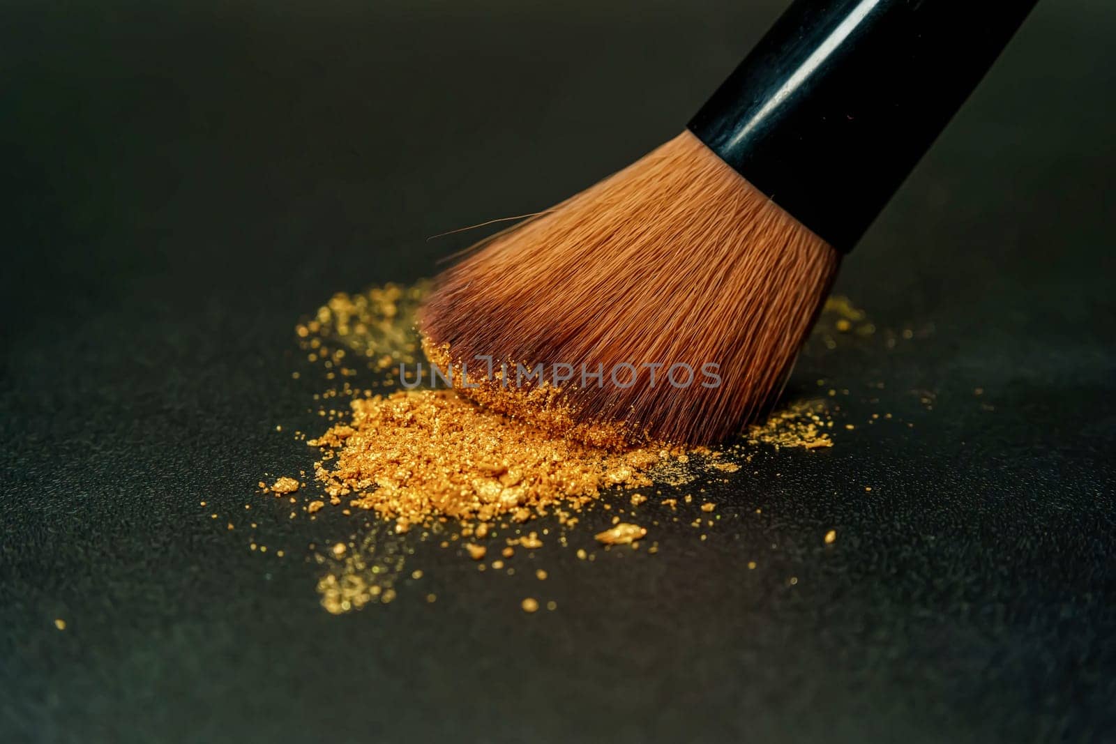 A delicate makeup brush, its bristles generously dusted with shimmering gold powder.