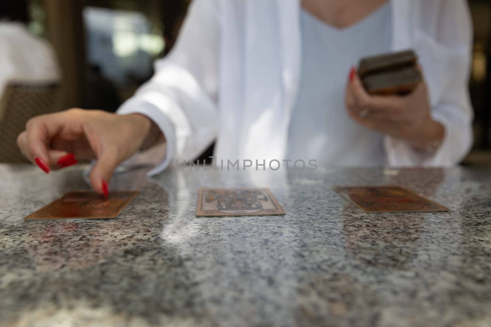 Close-up of woman spreading tarot cards on granite table, showing her red nails and white shirt. Copy space. fortune telling and divination by cards.lifestyle or spirituality content