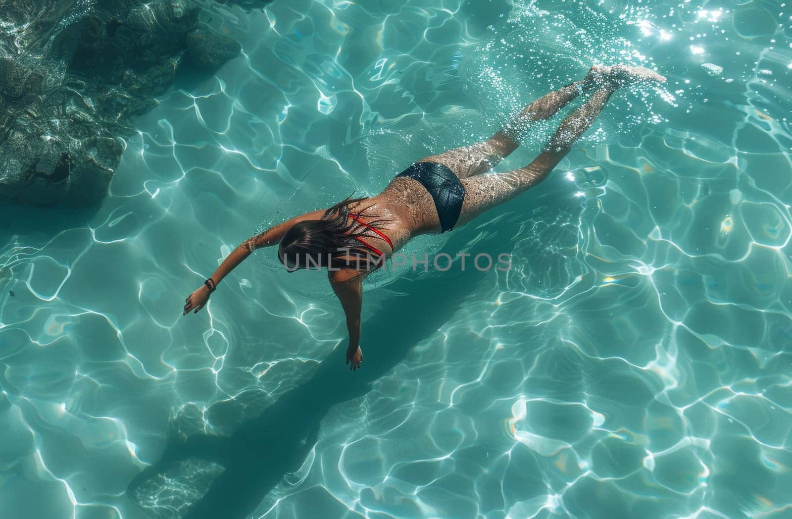 A graceful woman swims in a pool of crystal-clear blue water. She moves effortlessly, creating ripples that dance along the surface as she propels herself through the serene aquatic environment.