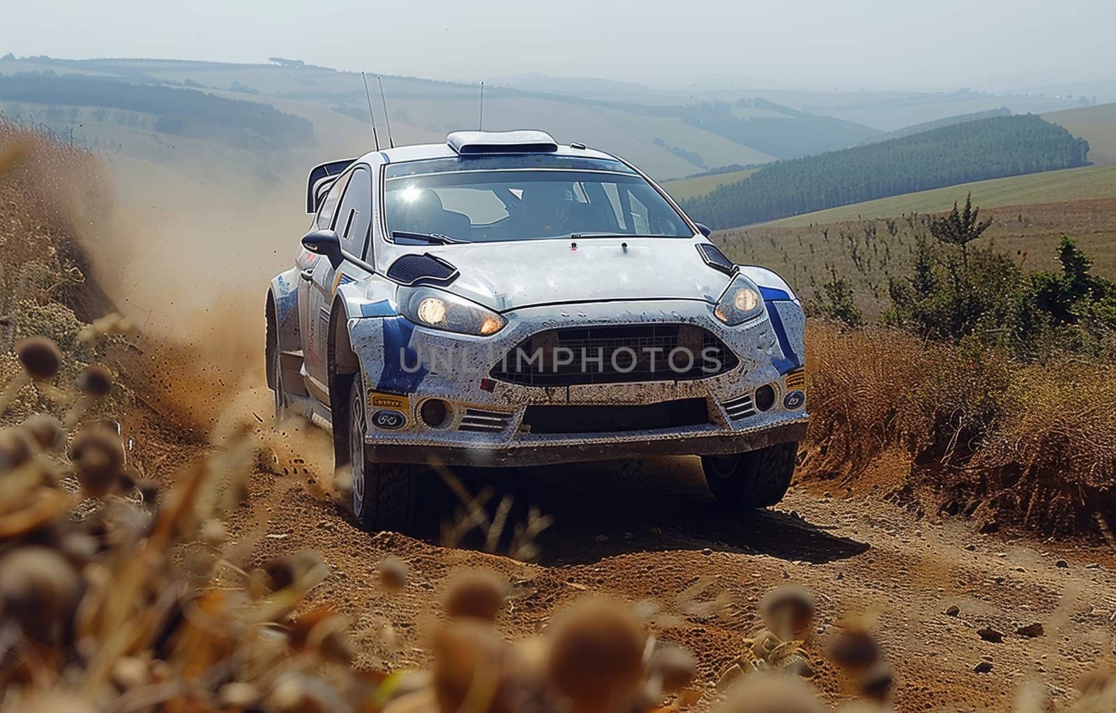 A powerful rally car speeds down a rugged dirt road, leaving a cloud of dust in its wake. The white Ford Fiuchay, adorned with blue and green accents, is driving with immense power and precision as it tackles the challenging terrain.