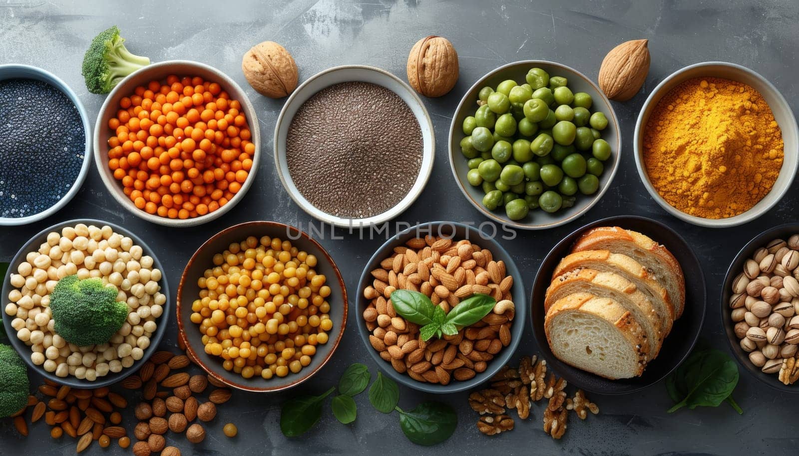 This image showcases a variety of high-fiber foods, arranged in a visually appealing manner on a gray surface. The assortment includes chickpeas, almonds, chia seeds, whole grain bread, pistachios, peas, and turmeric powder, highlighting the diverse range of options for incorporating fiber into ones diet.