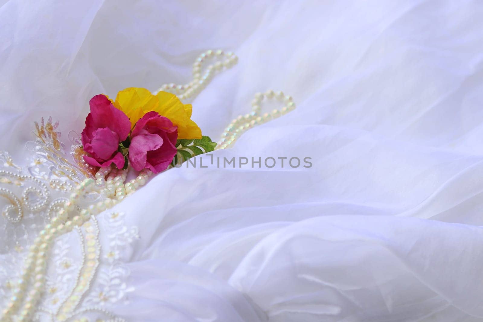 Delicate close-up of a wedding dress with roses, poppy and pearls