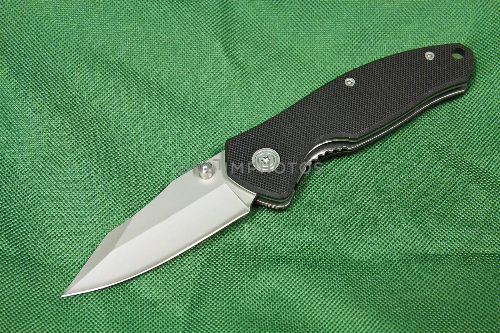 Folding knife with a black handle and lock on green canvas