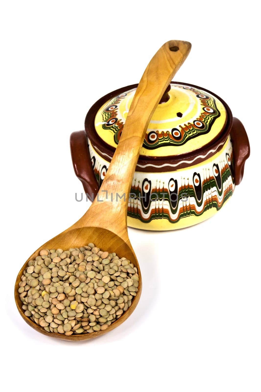 Wooden spoon full of raw lentils supported a color ceramic pot