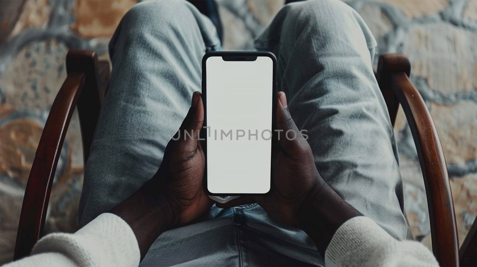 African American man holding smart phone with mockup white blank display, empty screen for app ads sitting on couch at home. Mobile applications technology concept, over shoulder close up view. top view