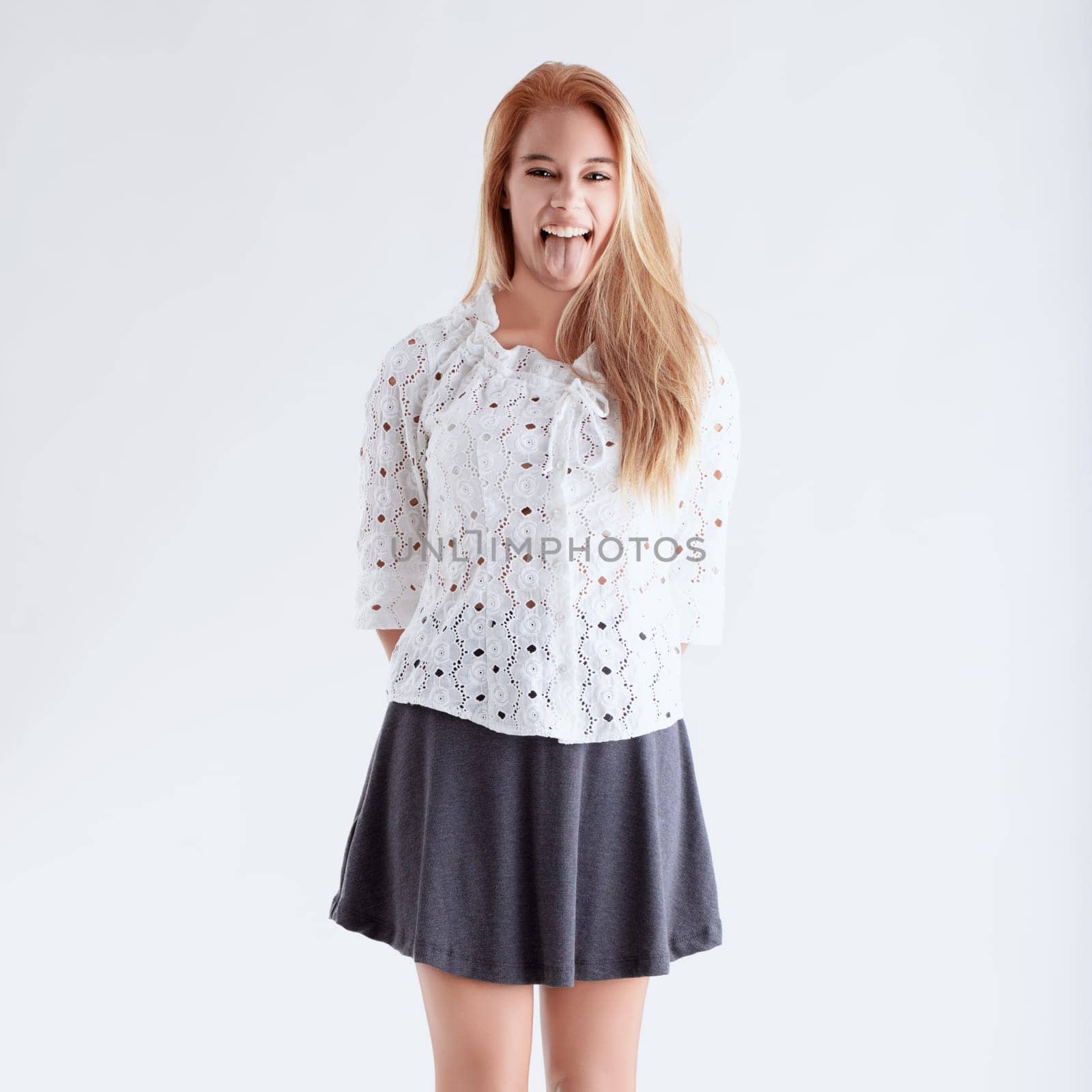 Cheerful young woman with long blond hair playfully sticks out her tongue against a white background in a studio