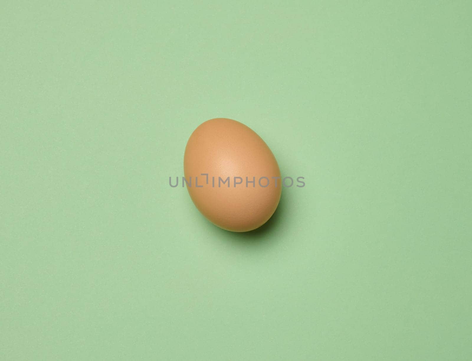 Raw brown egg on green background, top view