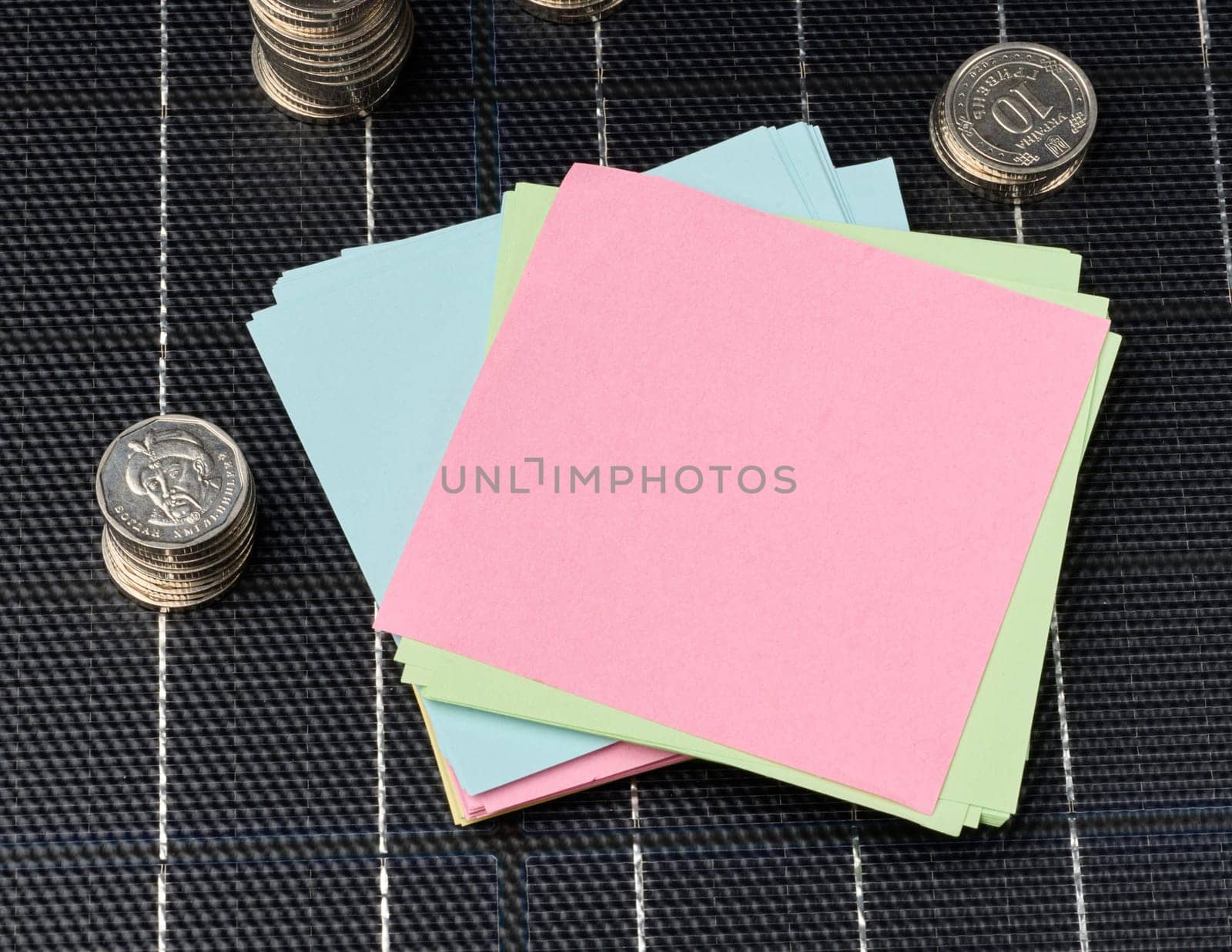 A stack of coins and paper stickers stands on a solar panel, budget savings when using renewable electricity