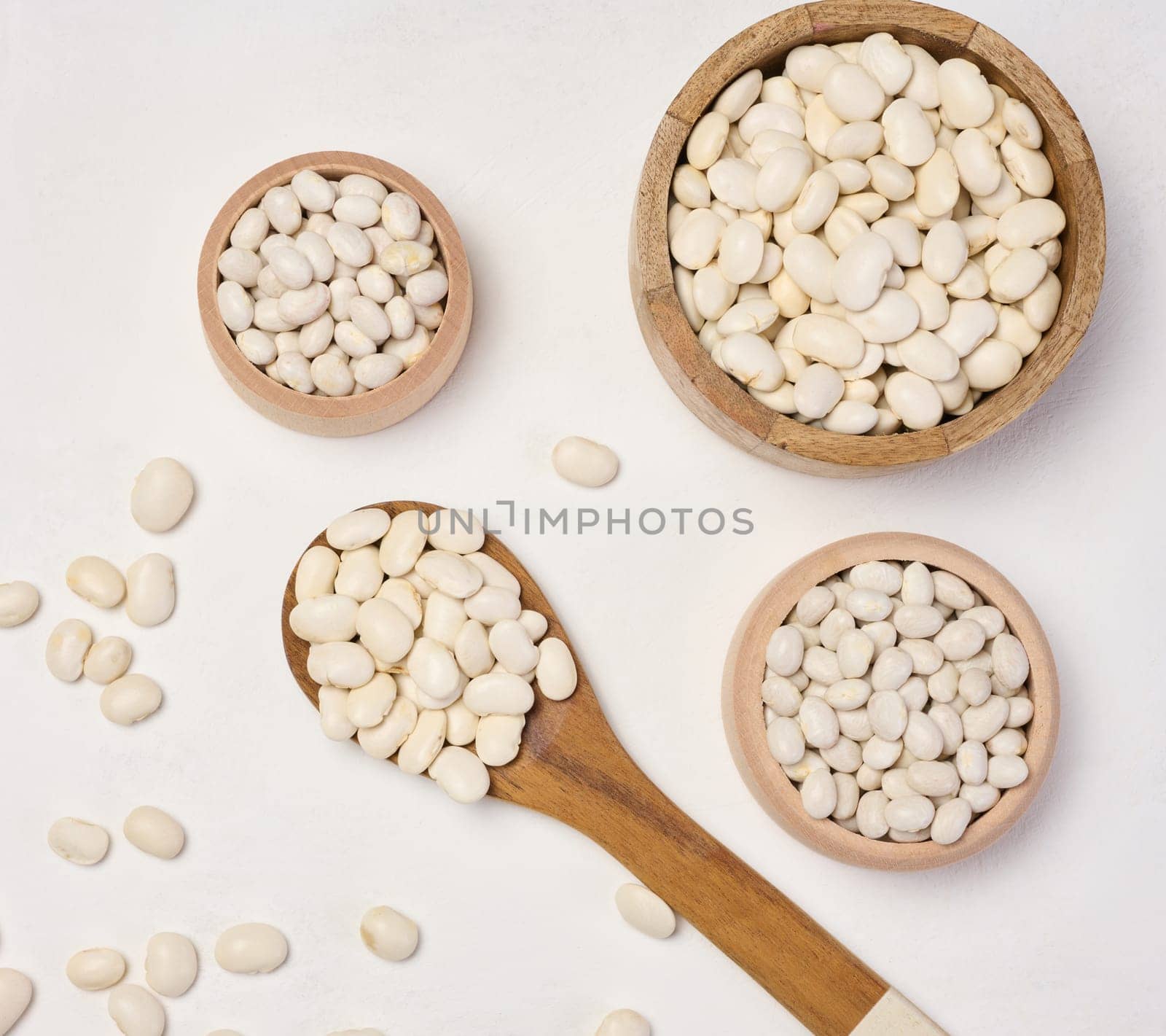 Raw white beans in a plate on the white table, top view.