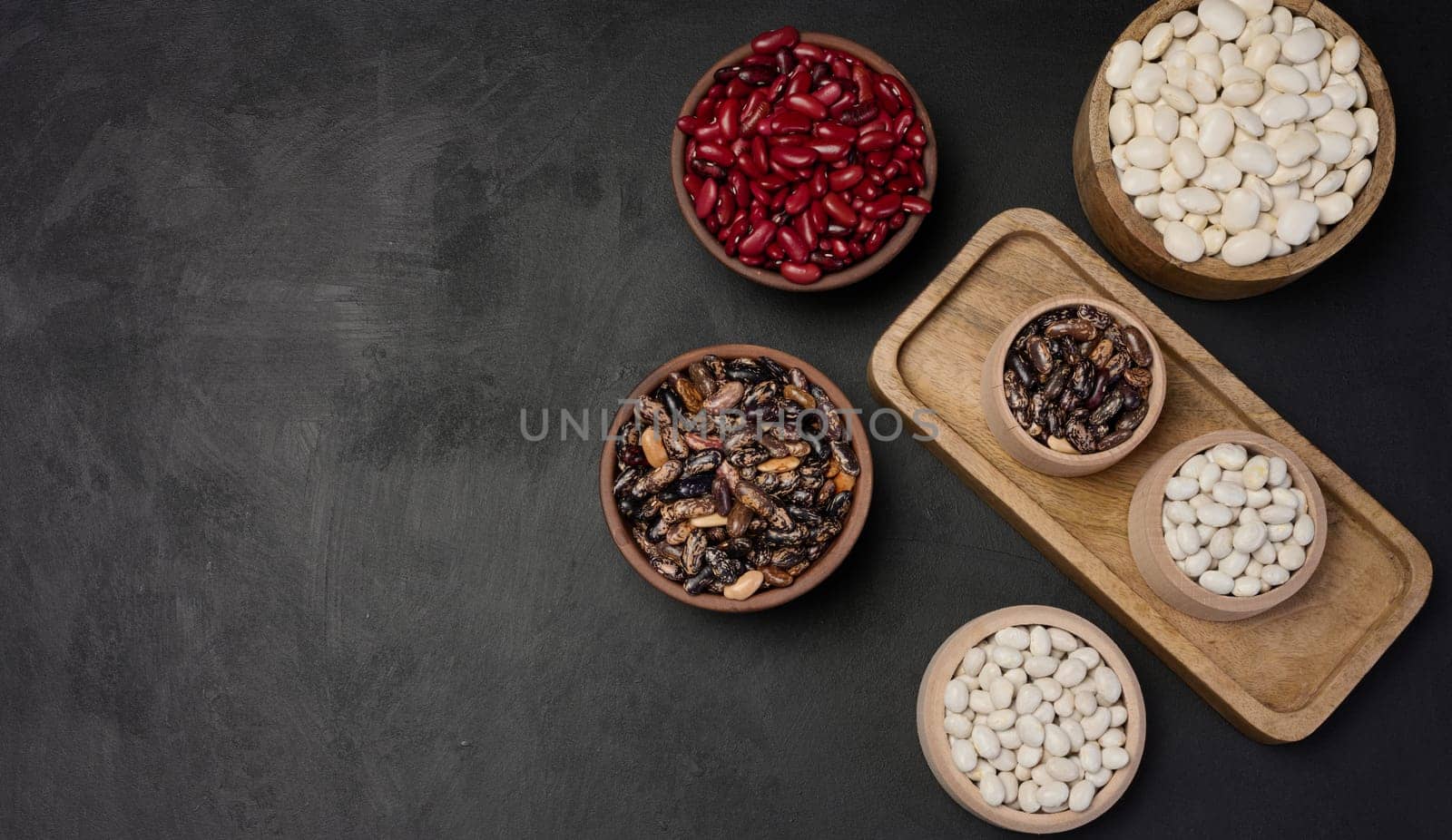 Raw white and red beans in a plate on a black table, top view. Assortment. Copy space