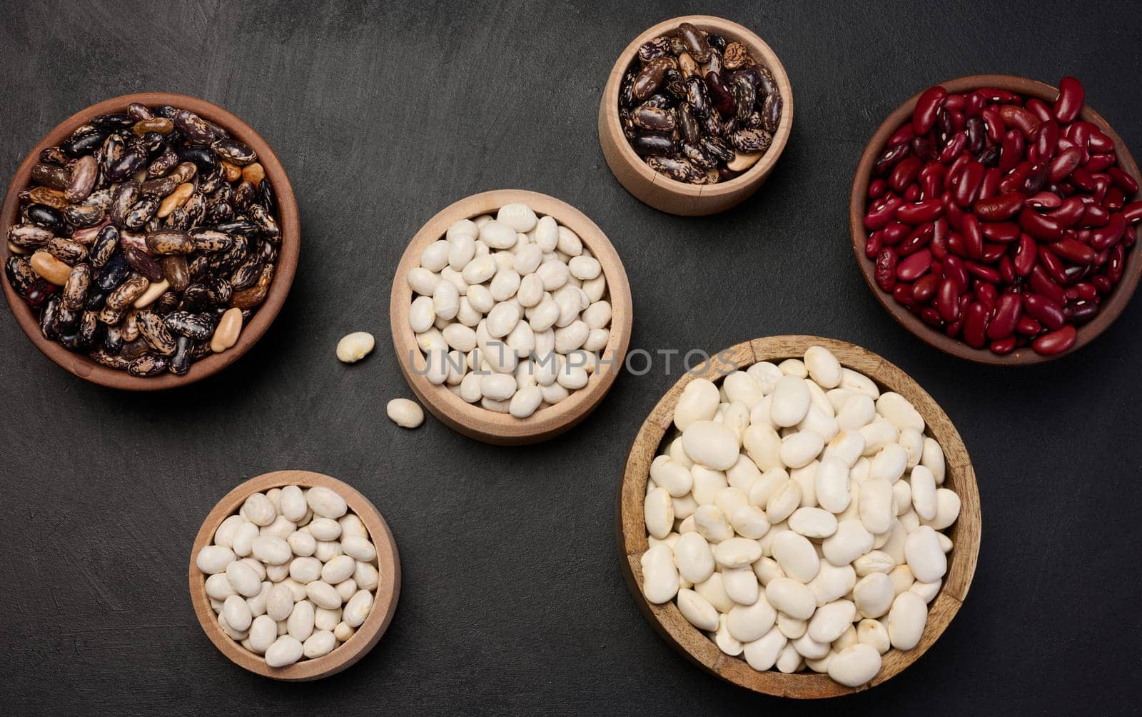 Raw white and red beans in a plate on a black table, top view. Assortment
