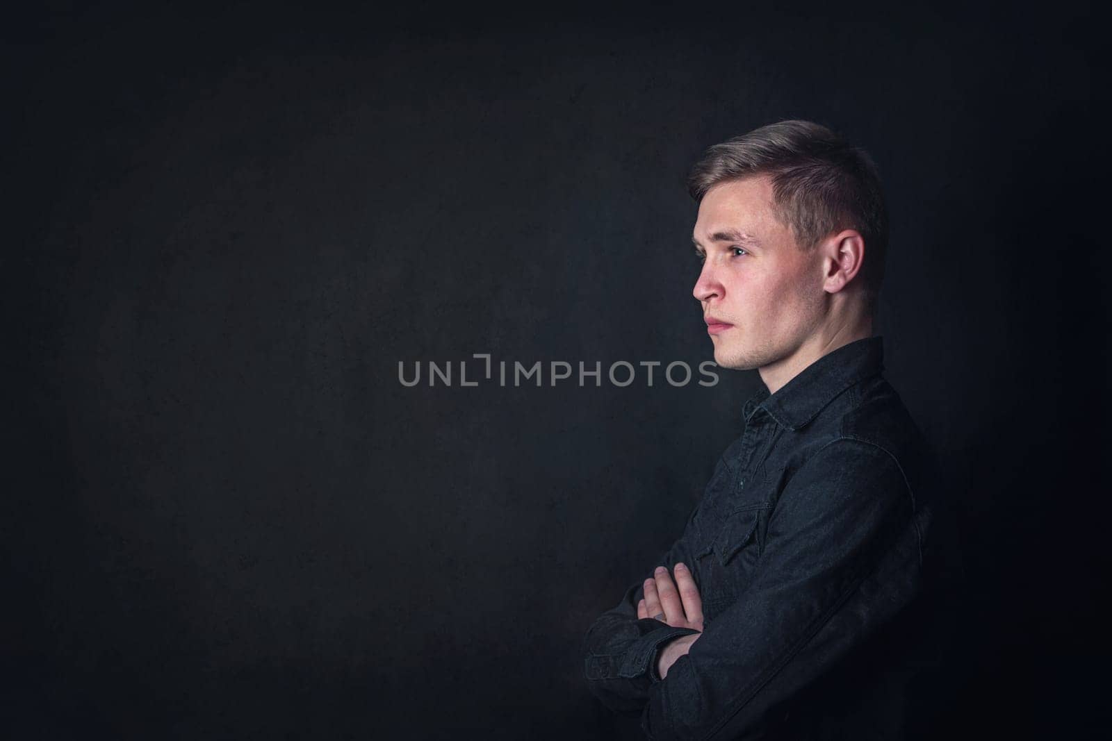 Serious contemplative young man side view portrait, looks pensive against a dark wall background. Male student reflects as have questions
