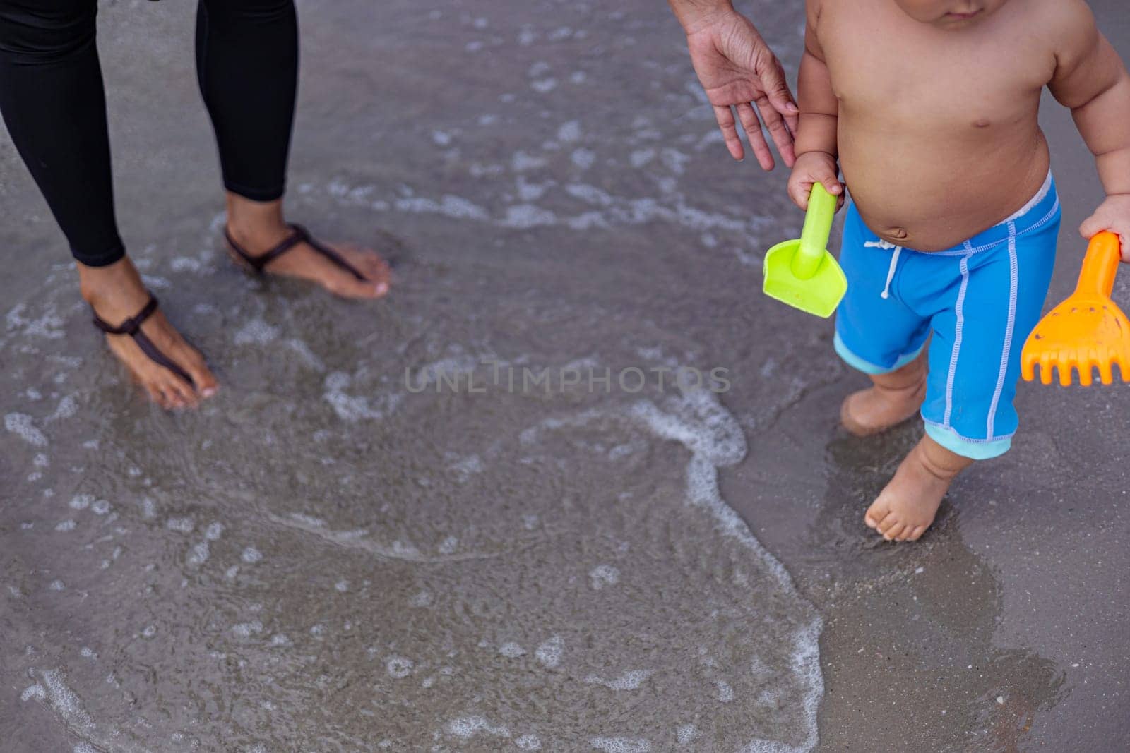 Little boy in blue shorts playing sand in the beach with his mother.