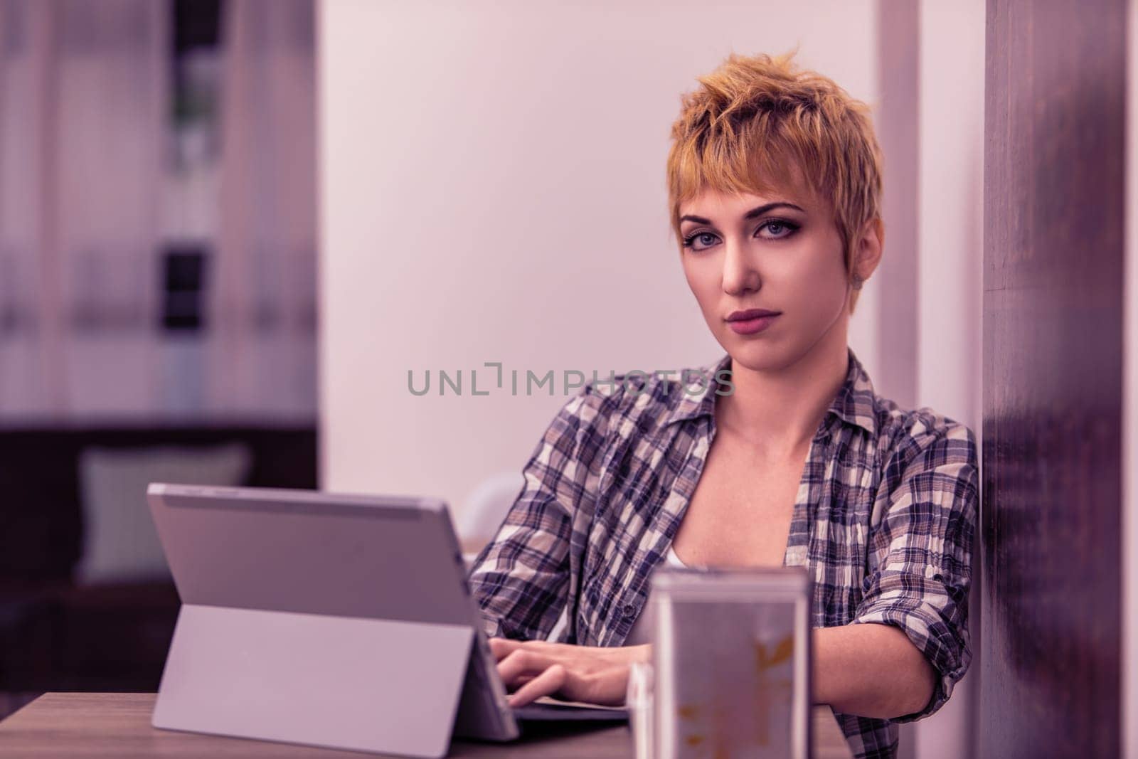 Confident young woman with short blonde hair works on a tablet in a modern office, showcasing focus and dedication in a startup setting
