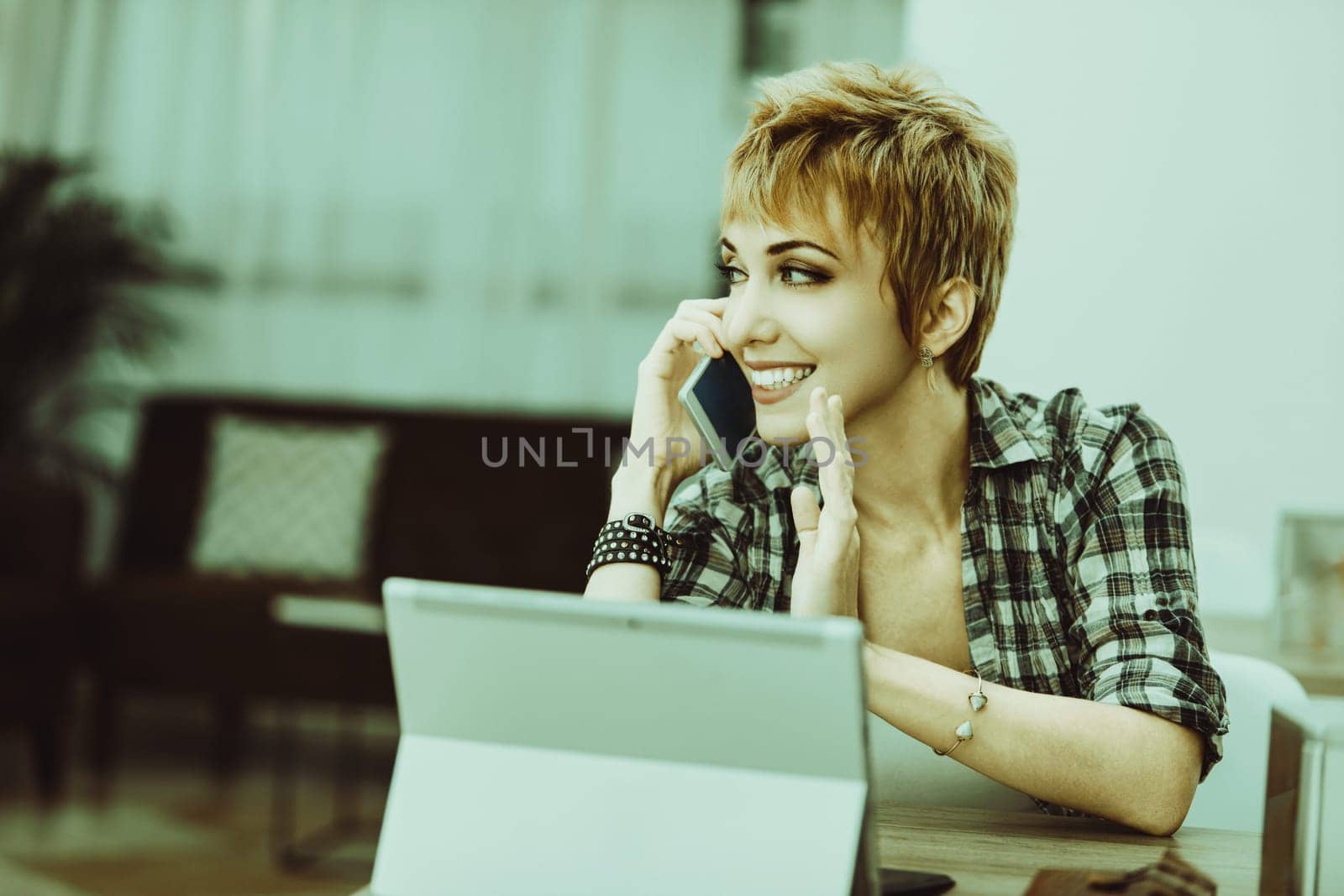Freelancer is working from home, talking on her smartphone and gesturing with her other hand while looking away from her laptop