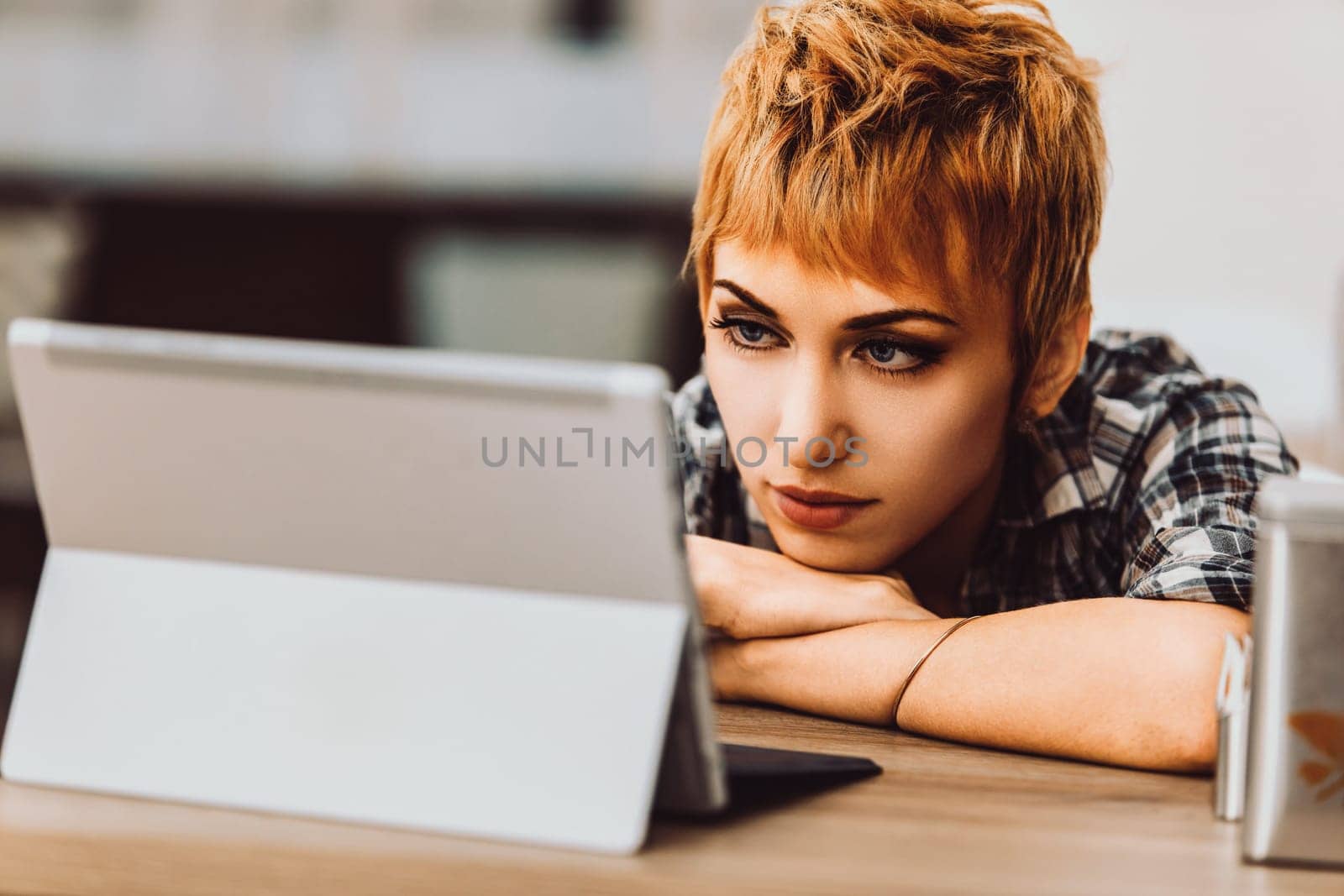 Young woman leaning on a desk in her home office, looking at a tablet screen with a serious expression, focusing on analyzing content