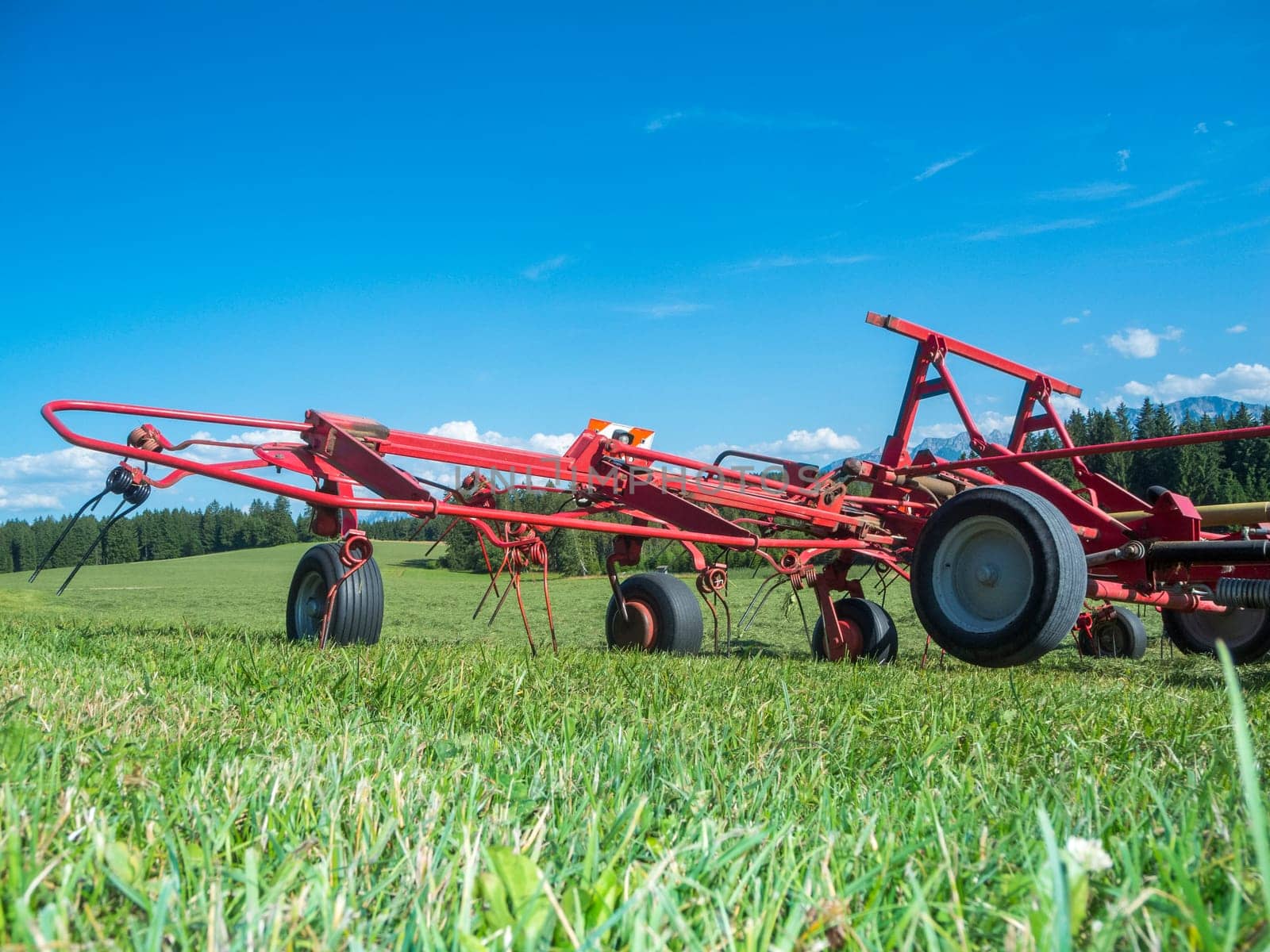 Ground level wide angle view of a red hay tedder on a pasture in the Bavarian Allgäu in summer.