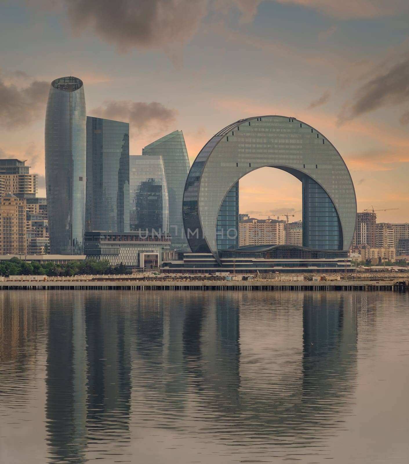 The Crescent Development Project features distinct modern architecture, including the Crescent Hotel, set against a beautiful sunset with reflections on the Caspian Sea in Baku, Azerbaijan