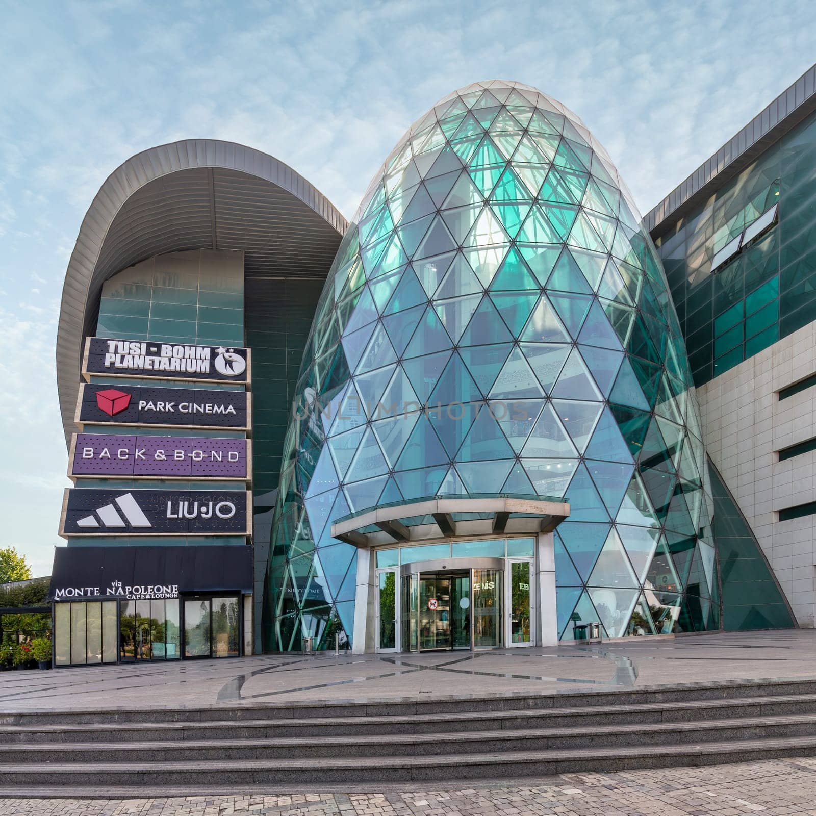 Baku, Azerbaijan - May 10 2024: Few people walk near the modern design of Park Bulvar Mall, on a sunny day, with clear blue skies overhead