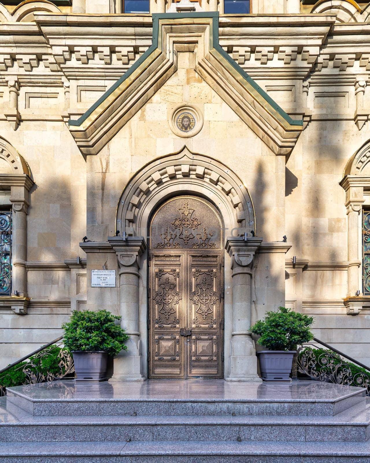 Close-up of Holy Myrrhbearers Cathedral entrance in Baku, Azerbaijan. Metal double doors with intricate designs lead to stone facade