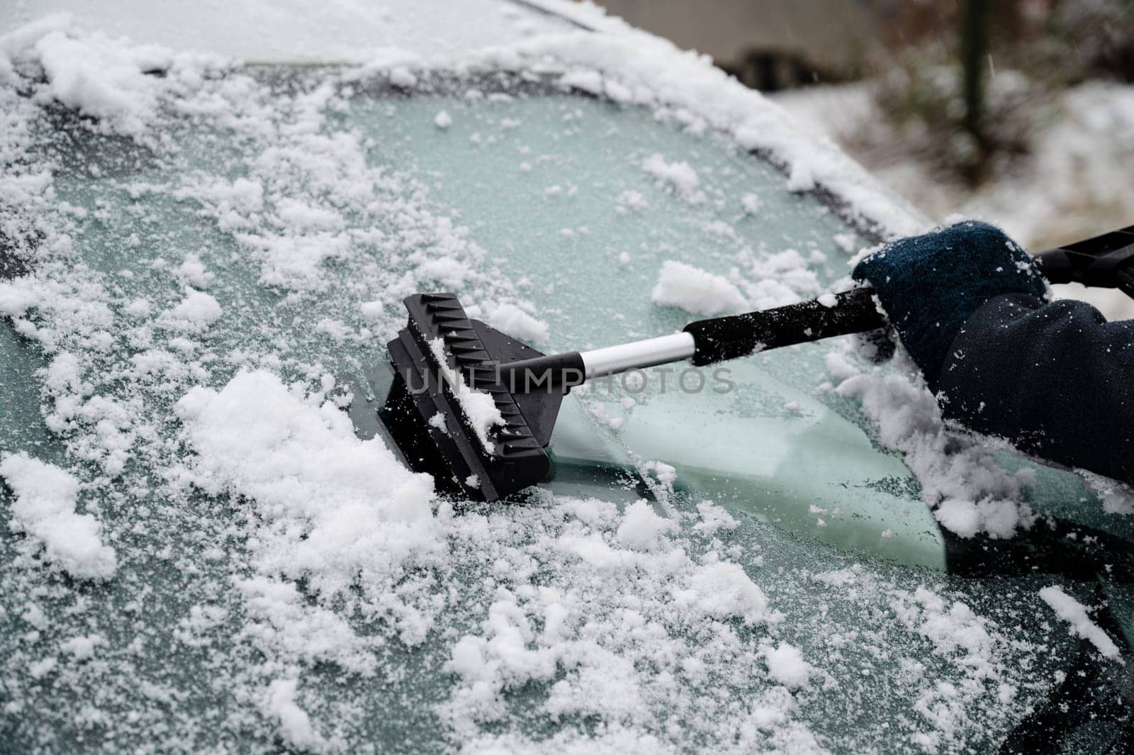 Driver is removing snow from car windshield with ice scraper and broom, clean car window from icy frost, winter season