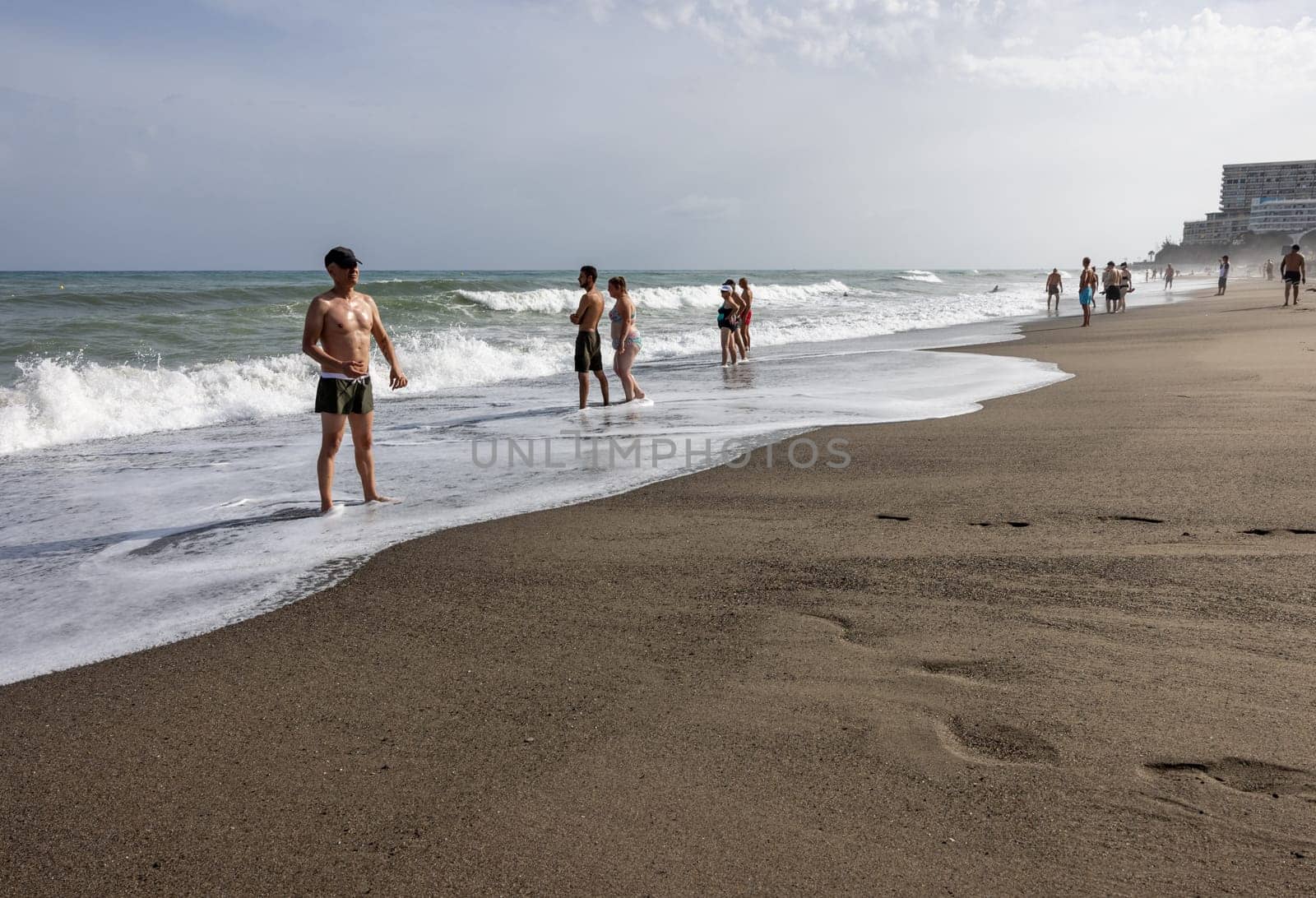 Torremolinos, Spain - September 14, 2023: Foamy sea waves and relaxing people on the sandy beach of Bajondillo in Torremolinos, Malaga, Costa del Sol, Spain