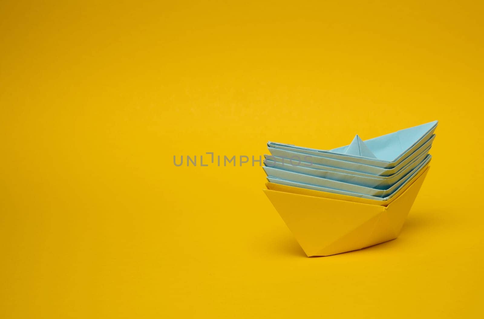 Paper boats on a yellow background, representing the concept of unity and achieving common goals.